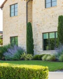 Russian Sage with purple flower spikes and ornamental grasses beside a stone home